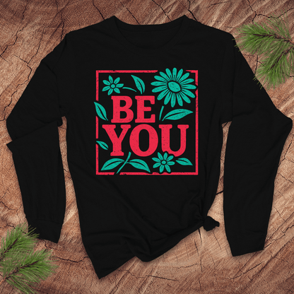 Black long-sleeve tshirt with 'BE YOU' text and floral design on a wooden surface