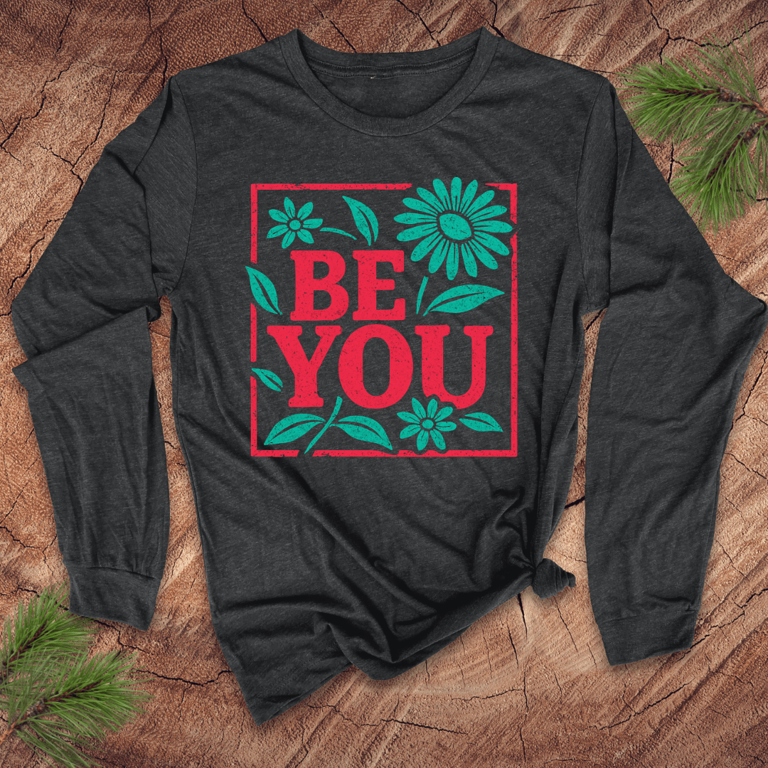Dark grey long-sleeve shirt with 'BE YOU' text and flowers on a wooden surface