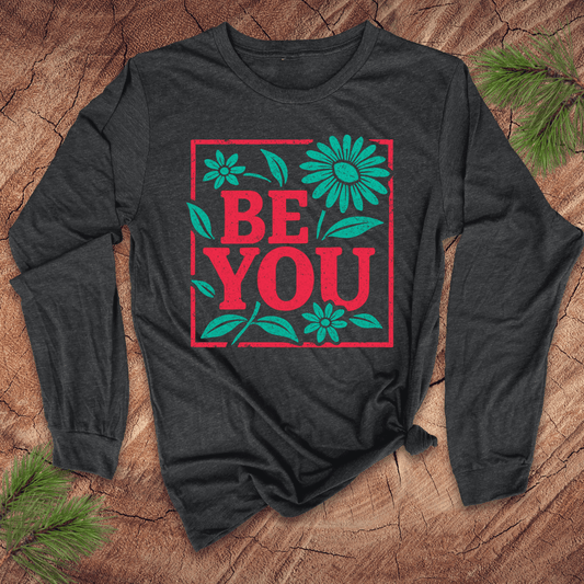Dark grey long-sleeve shirt with 'BE YOU' text and flowers on a wooden surface