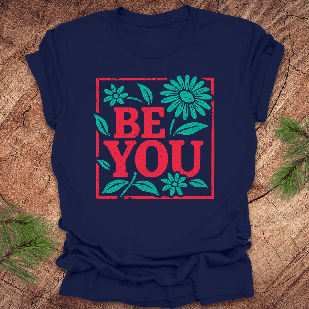 Navy blue t-shirt with 'BE YOU' text and floral design on a wooden surface