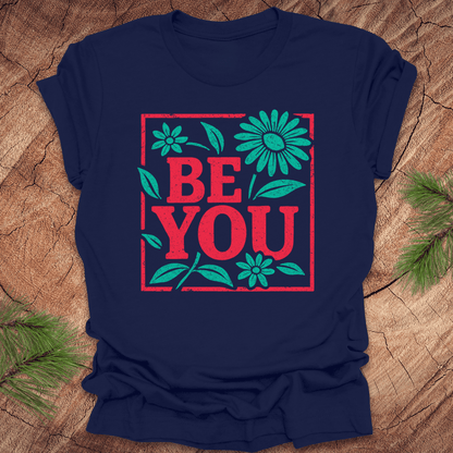 Navy blue t-shirt with 'BE YOU' text and floral design on a wooden surface
