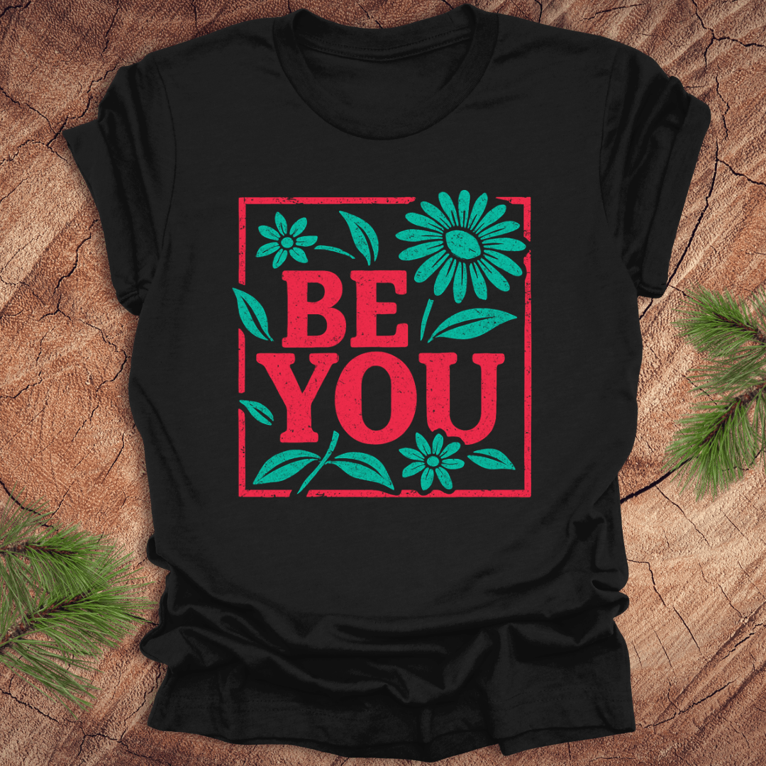 Black t-shirt with 'BE YOU' text and floral design on a wooden surface