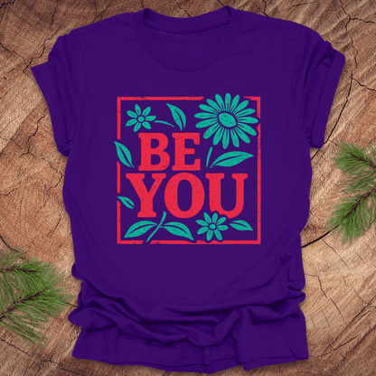 Purple t-shirt with 'BE YOU' text and floral design on a wooden surface
