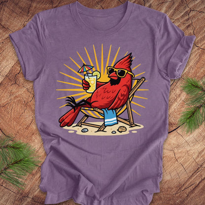 Purple t-shirt with a cardinal design holding a drink and sunglasses on a wooden surface.