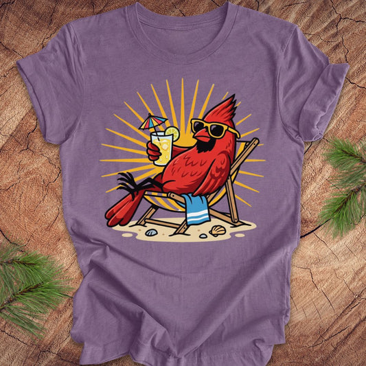 Purple t-shirt with a cardinal design holding a drink and sunglasses on a wooden surface.