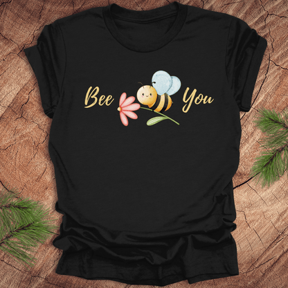 Black tshirt with a cute bee and the text, "bee you" on a wooden background.
