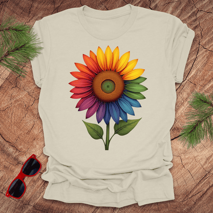 Beige tshirt with a bold rainbow sunflower graphic on a wood background.