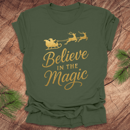 Green t-shirt with 'Believe in the Magic' text and Santa sleigh design on a wooden surface.