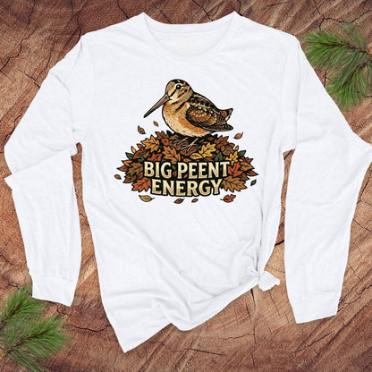 White long-sleeve shirt with a woodcock graphic and 'BIG PEENT ENERGY' text on a wooden surface.