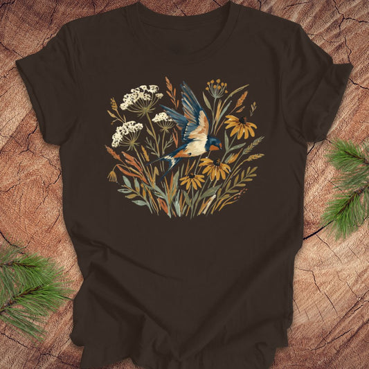 Brown t-shirt with watercolor flowers and a barn swallow in flight, on a wood background. 