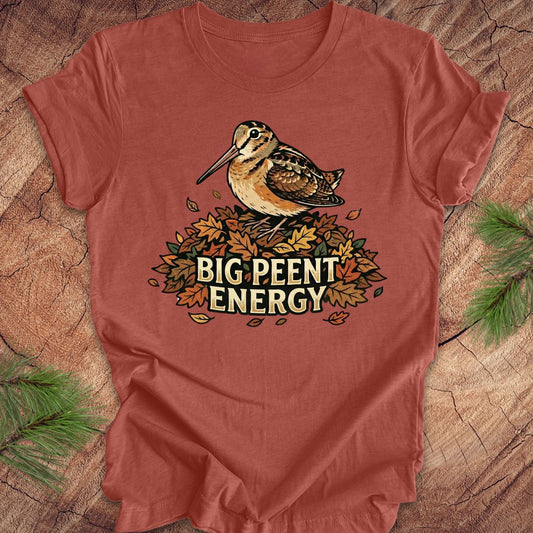  Clay colored t-shirt with a woodcock graphic and 'BIG PEENT ENERGY' text on a wooden surface.