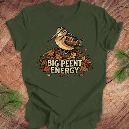 Green t-shirt with a woodcock graphic and 'BIG PEENT ENERGY' text on a wooden surface.