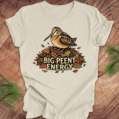 Beige t-shirt with a woodcock graphic and 'BIG PEENT ENERGY' text on a wooden surface.