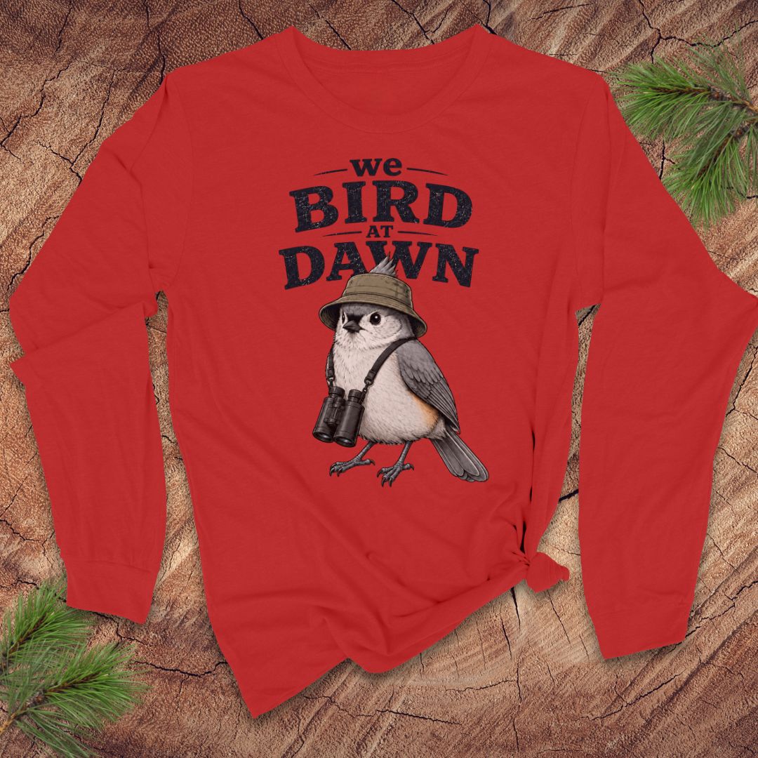 Red long-sleeve tshirt with a titmouse and text 'we bird at dawn' on a wood background.