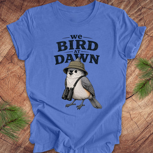 Blue t-shirt with a titmouse graphic and text 'we BIRD at DAWN' on a wooden surface.