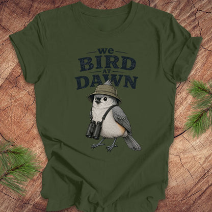 Green t-shirt with a titmouse graphic and text 'we BIRD at DAWN' on a wooden surface.