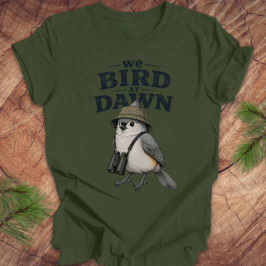 Green t-shirt with a titmouse graphic and text 'we BIRD at DAWN' on a wooden surface.