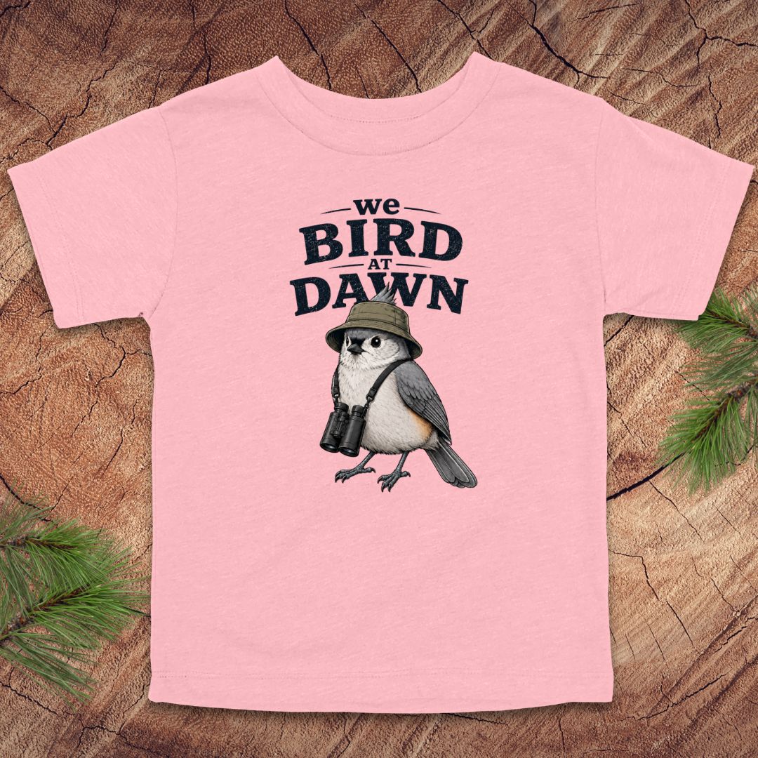 Pink t-shirt with a bird graphic and text on a wooden surface