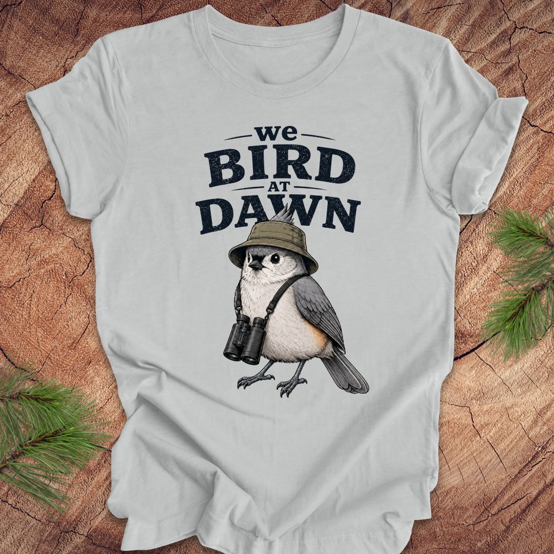 Gray t-shirt with a titmouse graphic and text 'we BIRD at DAWN' on a wooden surface.