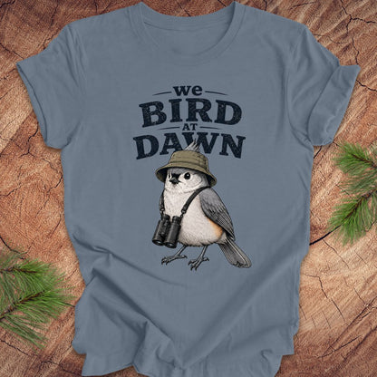 Blue t-shirt with a titmouse graphic and text 'we BIRD at DAWN' on a wooden surface.