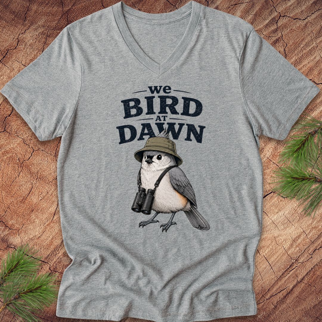 Gray t-shirt with a bird graphic and text 'we BIRD at DAWN' on a wooden surface.