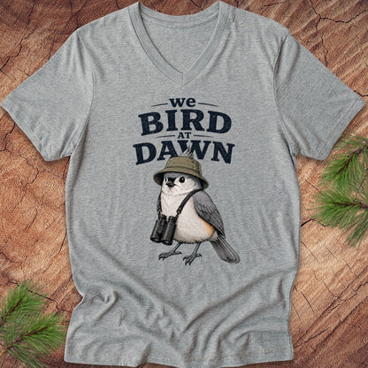 Gray t-shirt with a bird graphic and text 'we BIRD at DAWN' on a wooden surface.