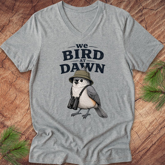Gray t-shirt with a bird graphic and text 'we BIRD at DAWN' on a wooden surface.
