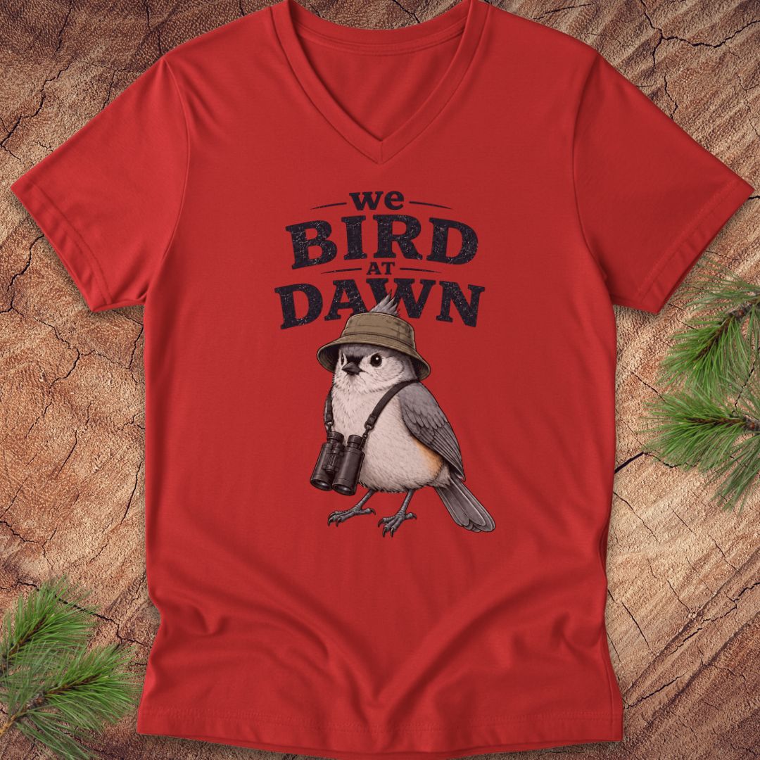 Red t-shirt with a bird graphic and text 'we BIRD at DAWN' on a wooden surface.
