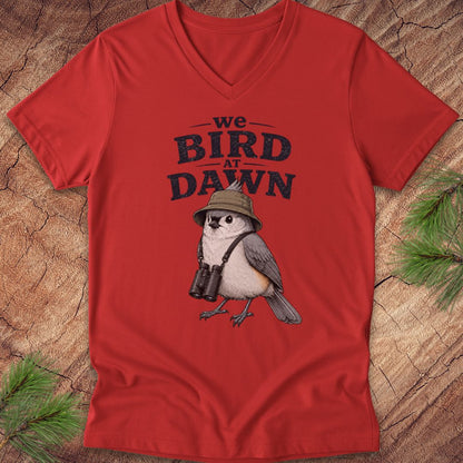 Red t-shirt with a bird graphic and text 'we BIRD at DAWN' on a wooden surface.