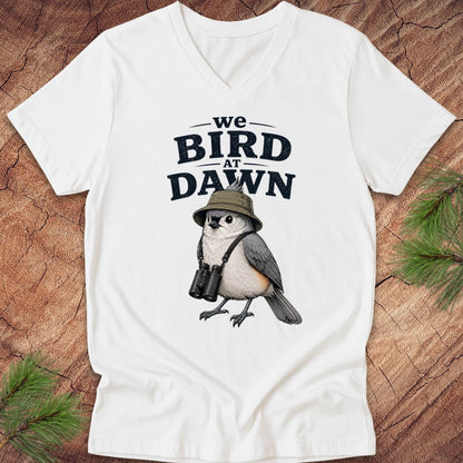 White t-shirt with a bird graphic and text 'we BIRD at DAWN' on a wooden surface.