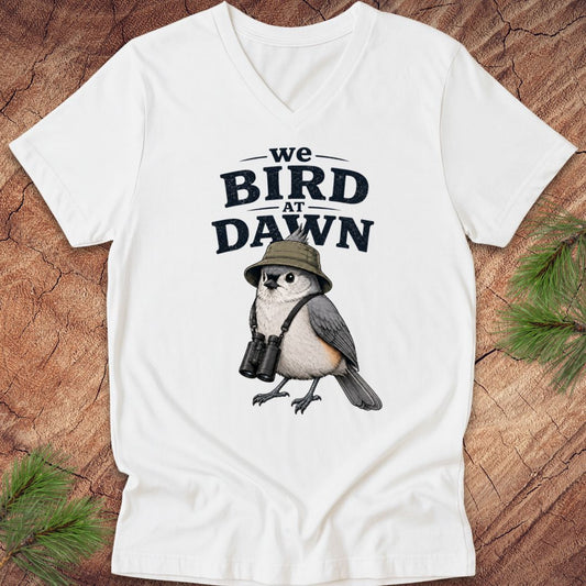 White t-shirt with a bird graphic and text 'we BIRD at DAWN' on a wooden surface.