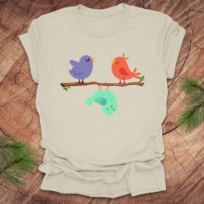 Beige blue t-shirt with cartoon birds on a branch with one upside down, on a wooden surface