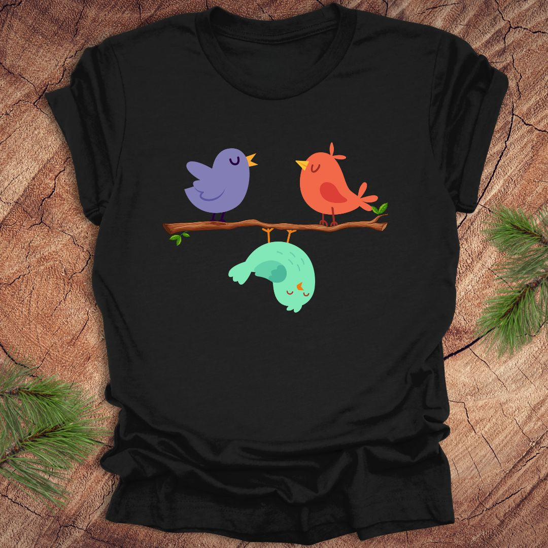 Black t-shirt with cartoon birds on a branch with one upside down, on a wooden surface