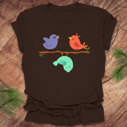 Brown t-shirt with cartoon birds on a branch with one upside down, on a wooden surface