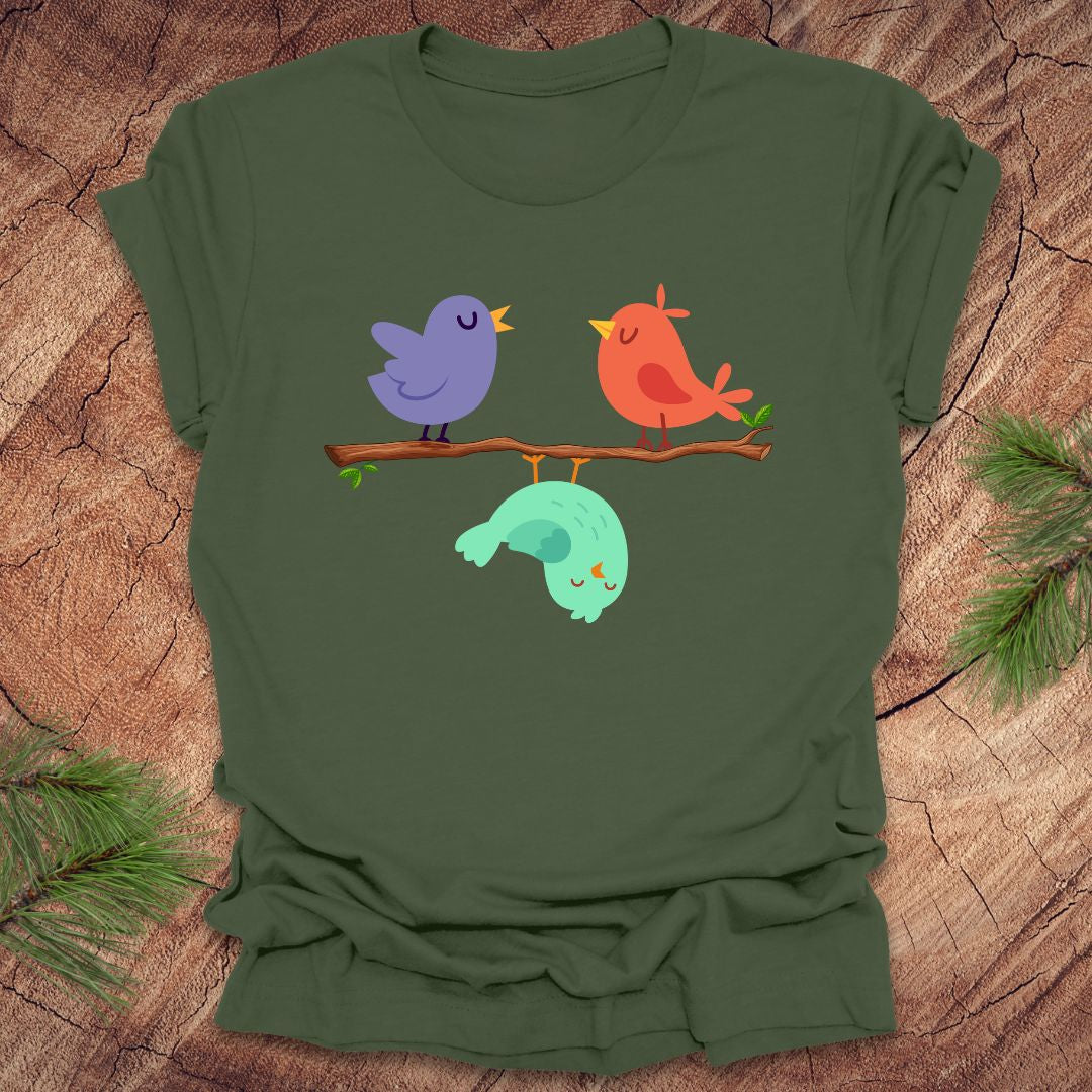 Green t-shirt with cartoon birds on a branch with one upside down, on a wooden surface