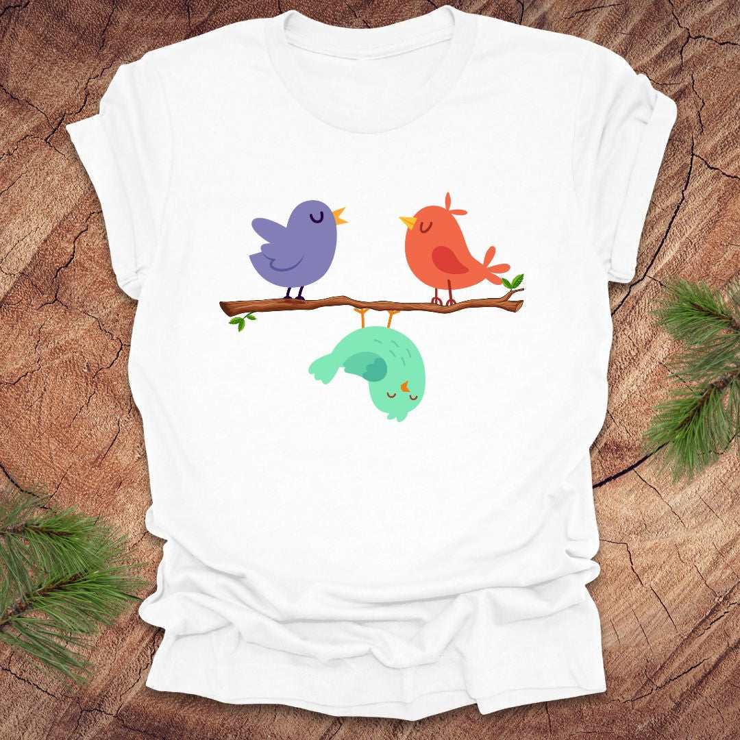 White t-shirt with cartoon birds on a branch with one upside down, on a wooden surface