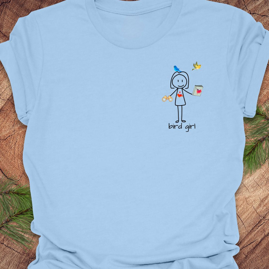 Baby blue close up t-shirt with a small stick figure and text, 'Bird Girl' on the left pocket side on a wooden surface