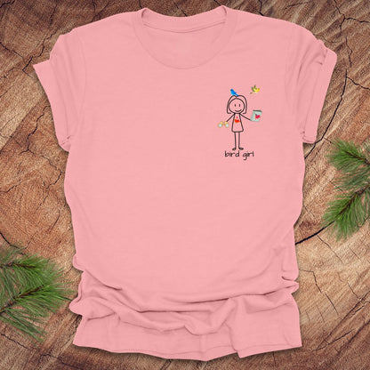 Pink t-shirt with a small stick figure and text, 'Bird Girl' on the left pocket side on a wooden surface