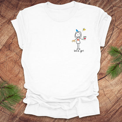 White t-shirt with a small stick figure and text, 'Bird Girl' on the left pocket side on a wooden surface