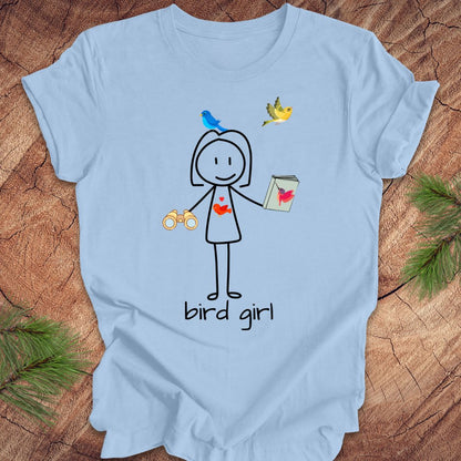 Light blue t-shirt with a stick figure design labeled 'bird girl' on a wooden surface.