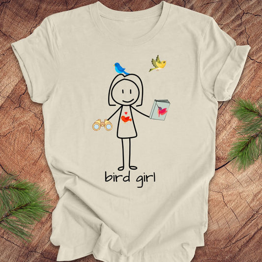 Beige t-shirt with a stick figure design labeled 'bird girl' on a wooden surface.