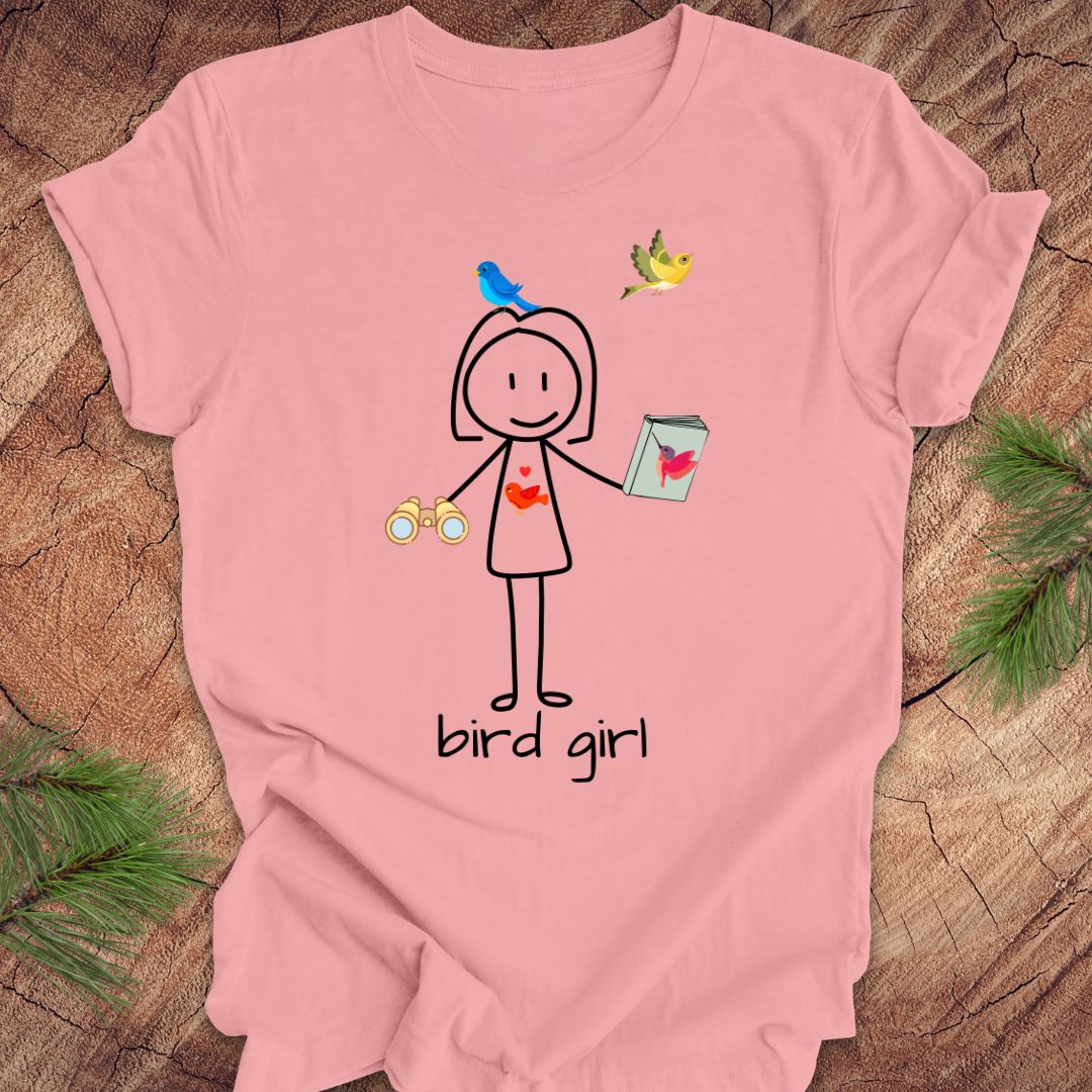 Pink t-shirt with a stick figure design labeled 'bird girl' on a wooden surface.
