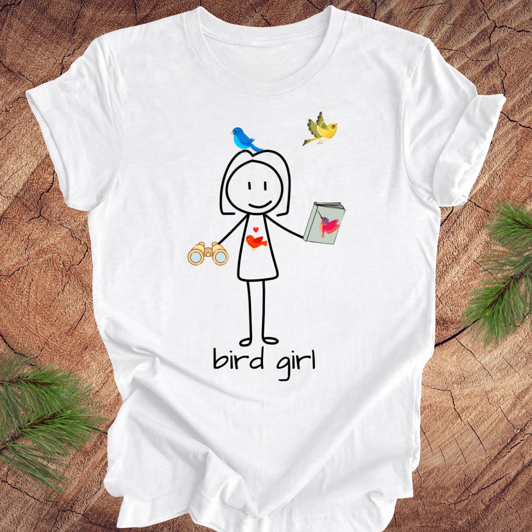 White t-shirt with a stick figure design and 'bird girl' text on a wooden surface.
