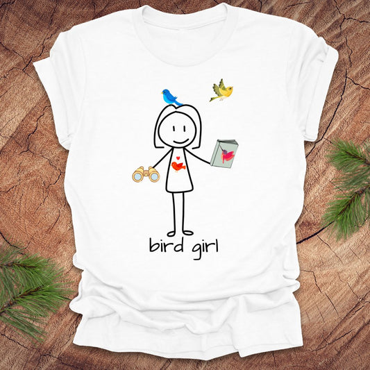 White t-shirt with a stick figure design holding binoculars and a bird book, with birds flying labeled 'bird girl' on a wooden surface.