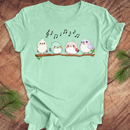 Mint green t-shirt with cartoon birds and musical notes on a wooden surface