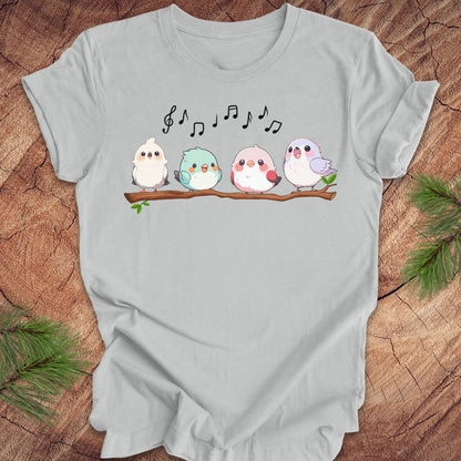 Light gray t-shirt with cartoon birds and musical notes on a wooden surface