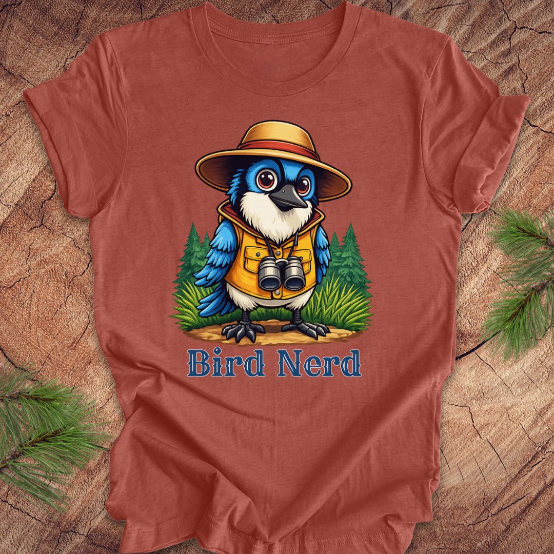 A rust-colored t-shirt featuring a colorful cartoon bird wearing a safari hat and vest with the text 'Bird Nerd' underneath, displayed flat on a rustic wood background with pine branches.