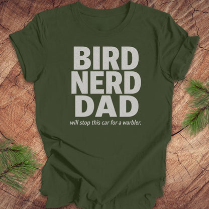 Green t-shirt with 'BIRD NERD DAD' text on a wooden surface with pine branches.