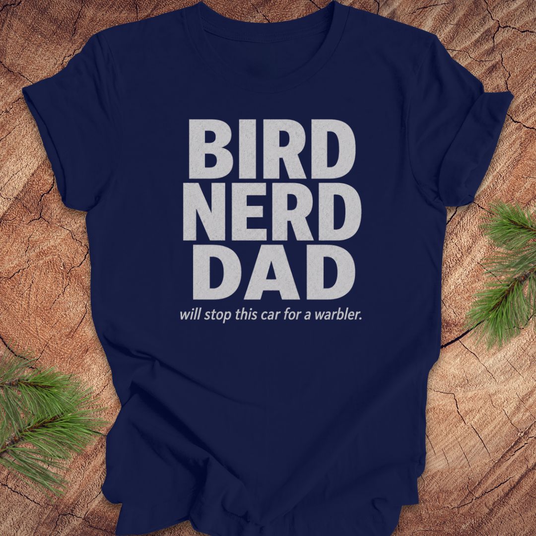 Navy blue t-shirt with 'BIRD NERD DAD' text on a wooden surface with greenery.