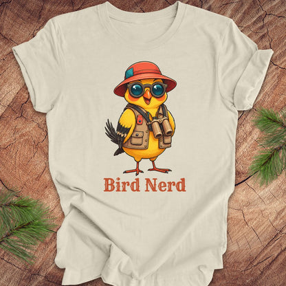 Beige t-shirt with a cartoon bird wearing a hat and sunglasses, labeled 'Bird Nerd', on a wooden surface.